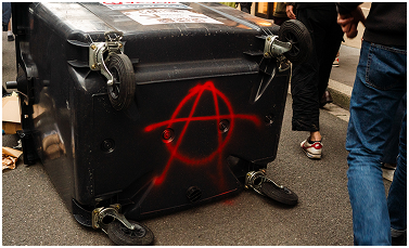 Photographie des poubelles retournées et d'un symbole antifa lors d'une manifestation